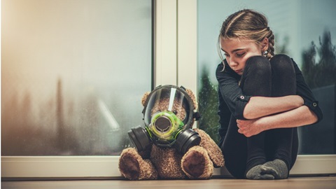 Une fillette inquiète assise à côté de son ours en peluche qui porte un masque contre la pollution